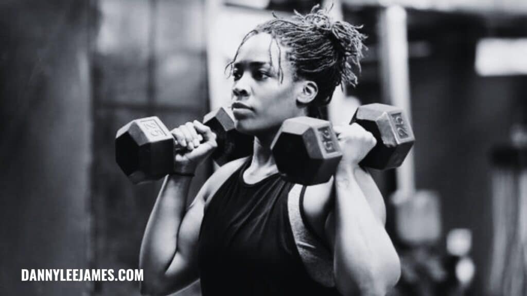 Fit strong woman doing dumbbell shoulder press in black and white.